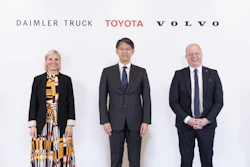 Three business executives pose together at a corporate event with Daimler Truck, Toyota, and Volvo logos displayed behind them