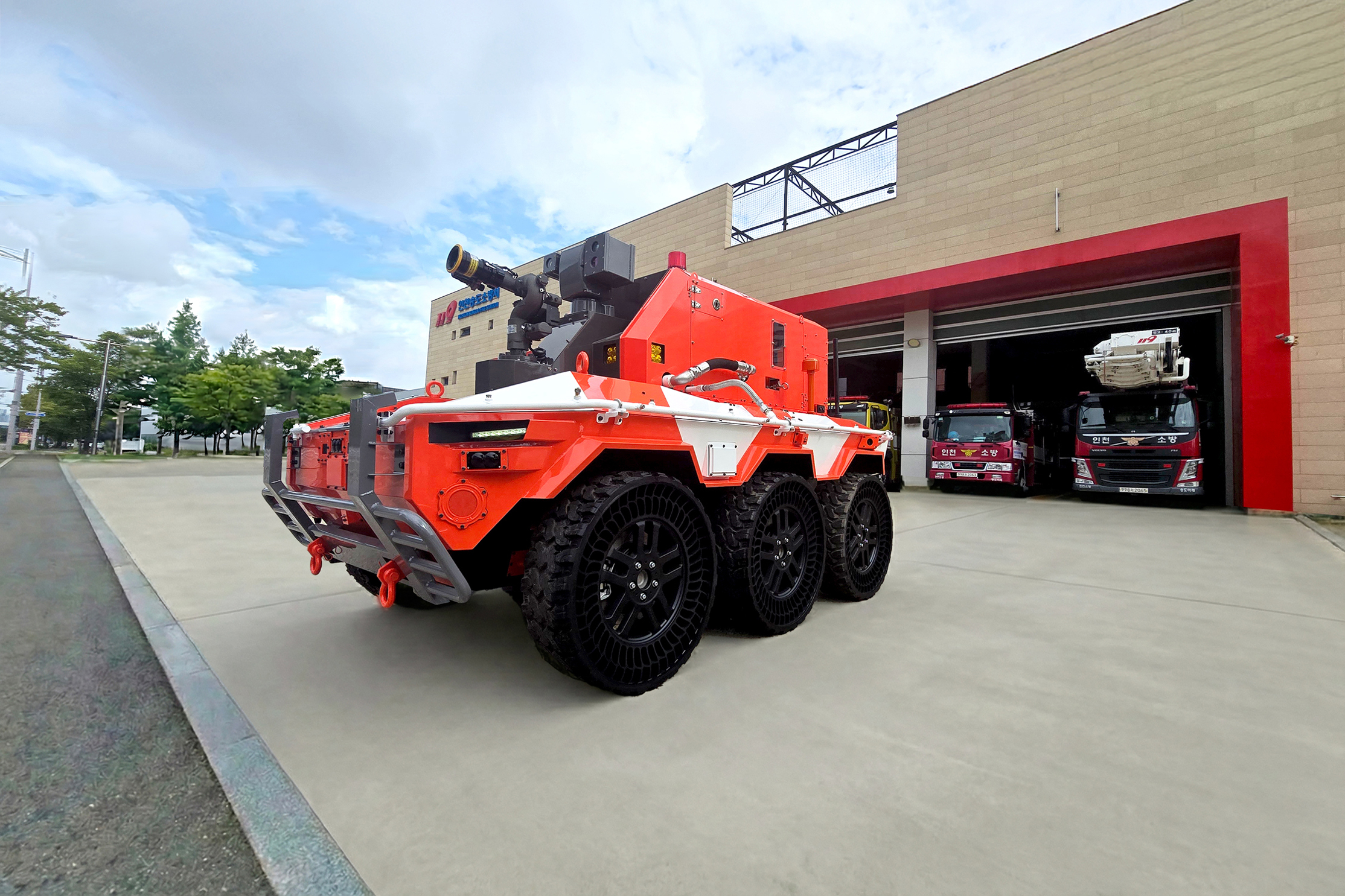 Orange and white autonomous firefighting robot with six wheels parked outside a fire station garage bay