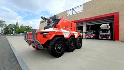Orange and white autonomous firefighting robot with six wheels parked outside a fire station garage bay