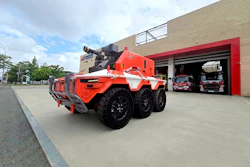 Orange and white autonomous firefighting robot with six wheels parked outside a fire station garage bay