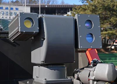 Military electro-optical infrared sensor turret with multiple camera lenses mounted outdoors near a building