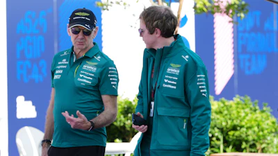 Two Aston Martin F1 team members in teal branded apparel having a conversation at a paddock event
