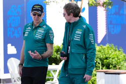 Two Aston Martin F1 team members in teal branded apparel having a conversation at a paddock event