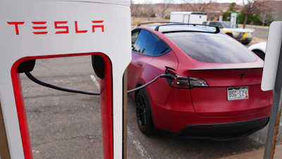 Red Tesla electric vehicle charging at a white Tesla Supercharger station in a parking lot