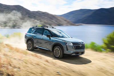 Silver Nissan SUV driving on dusty terrain with mountain lake landscape in background