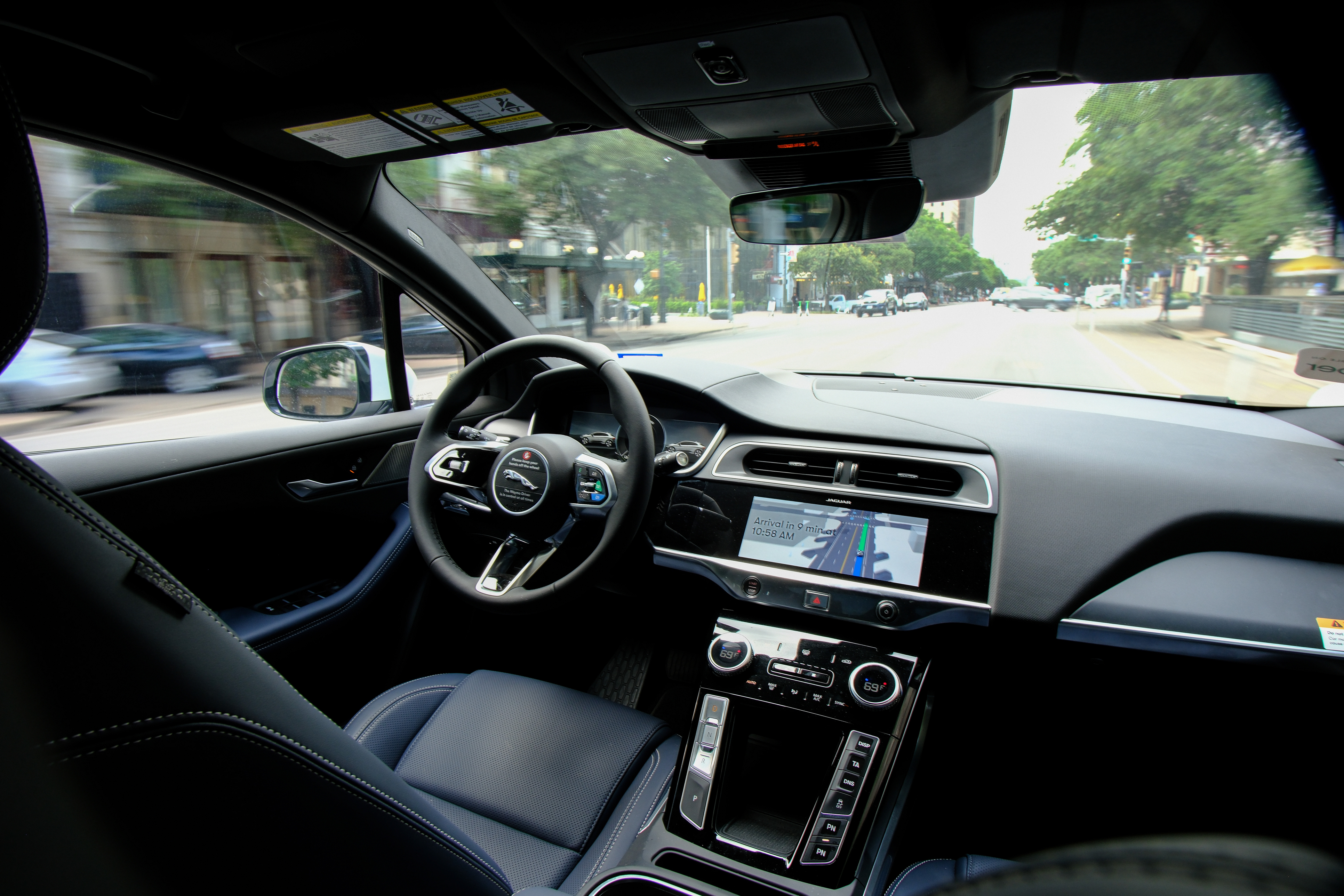Luxury car interior dashboard with steering wheel and navigation display while driving on urban street