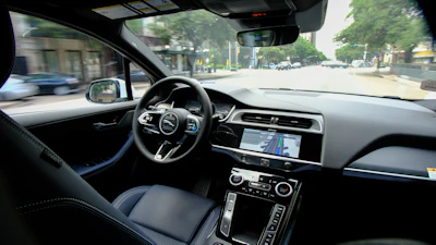Luxury car interior dashboard with steering wheel and navigation display while driving on urban street