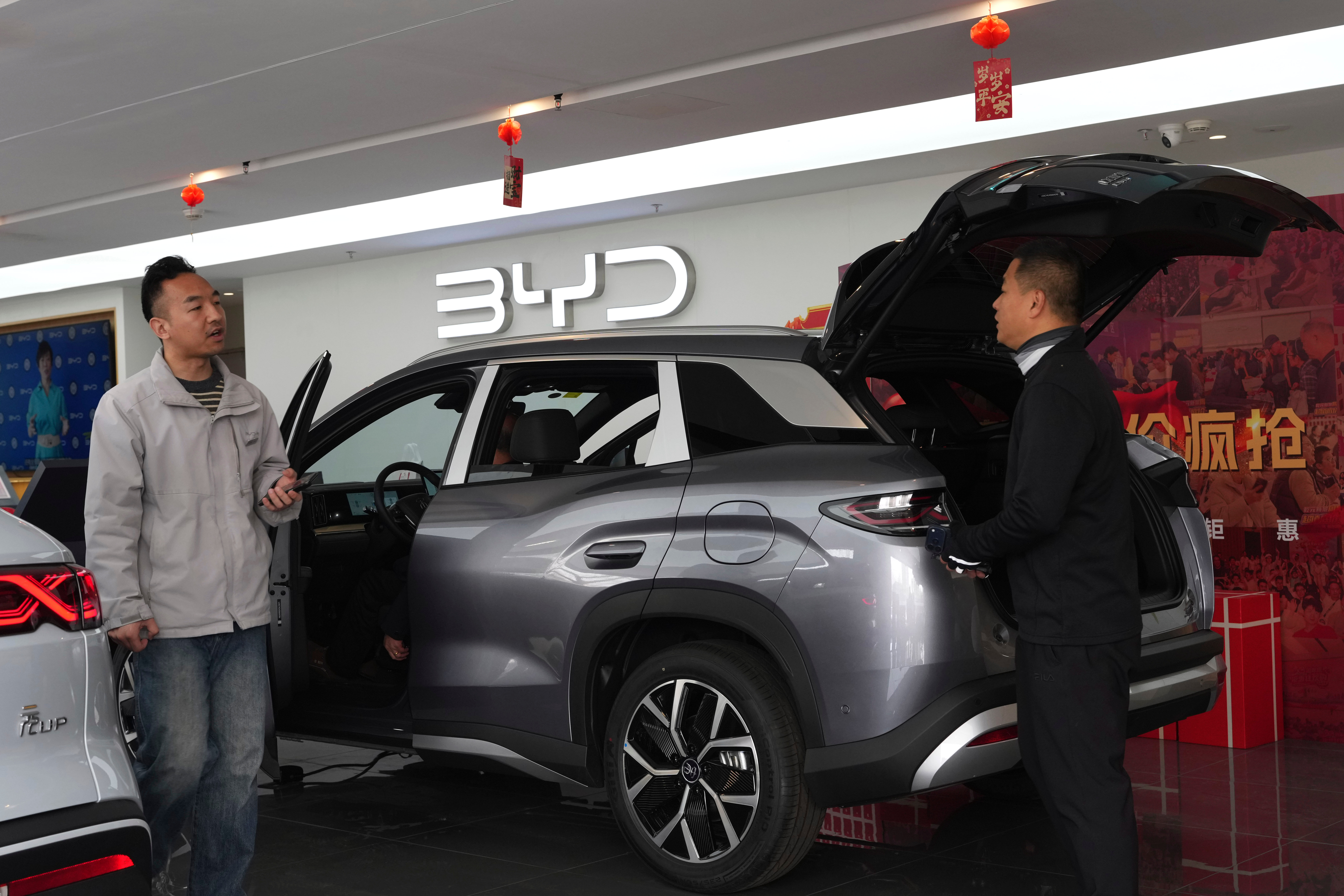 BYD electric SUV displayed at showroom with sales representatives and red decorative elements