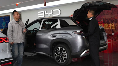 BYD electric SUV displayed at showroom with sales representatives and red decorative elements