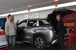 BYD electric SUV displayed at showroom with sales representatives and red decorative elements
