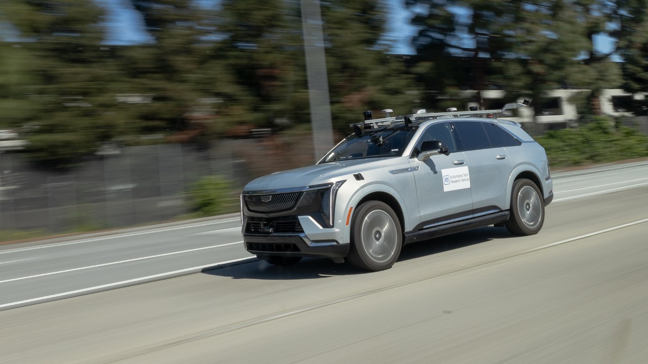 Light blue Cadillac Lyriq electric SUV driving on a sunny road with trees in background
