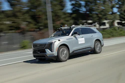 Light blue Cadillac Lyriq electric SUV driving on a sunny road with trees in background