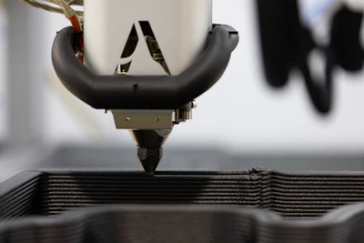 3D printer nozzle extruding material onto layered print with blurred background