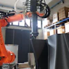 Kuka industrial robotic arm with orange frame operating in warehouse with blue shelving and cardboard boxes