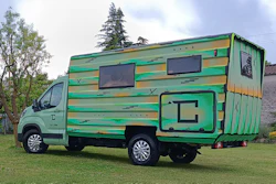 Green and yellow striped motorhome parked on grass with trees in background