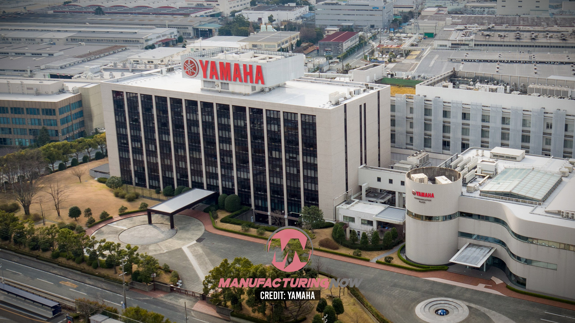 Yamaha manufacturing facility with red logo signage on white rooftop overlooking industrial complex