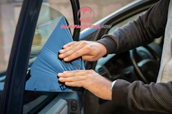 Person applying blue window tint film to car window during installation