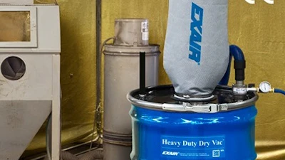 Industrial sandblasting equipment setup with blue EMCO drum unit and gray cabinet blaster in workshop