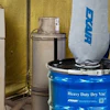 Industrial sandblasting equipment setup with blue EMCO drum unit and gray cabinet blaster in workshop