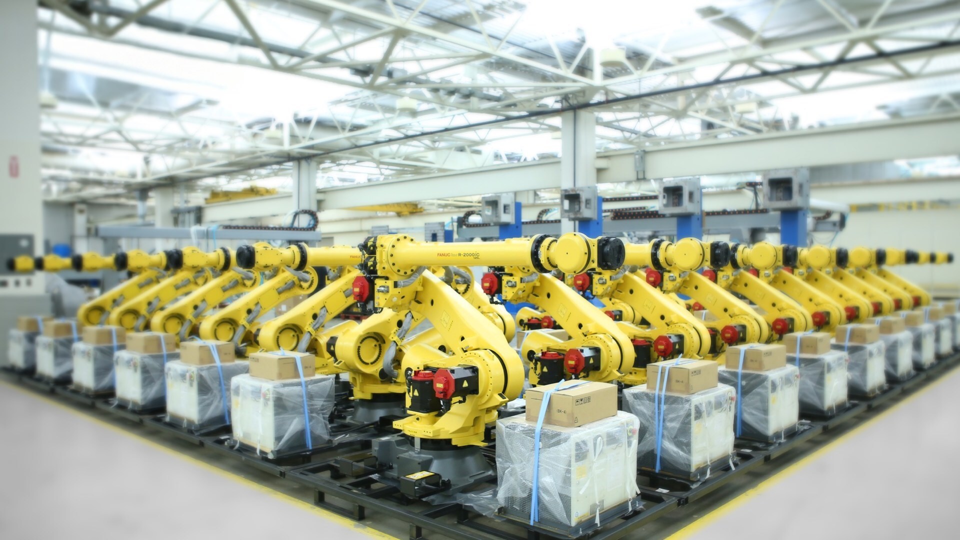 Factory floor with rows of yellow industrial robotic arms positioned on assembly line under bright ceiling lights