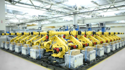 Factory floor with rows of yellow industrial robotic arms positioned on assembly line under bright ceiling lights