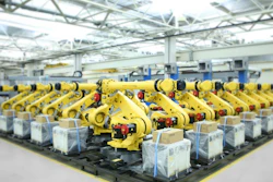 Factory floor with rows of yellow industrial robotic arms positioned on assembly line under bright ceiling lights