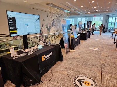 Corporate event exhibition space with branded display tables, digital screens, and attendees in modern office setting