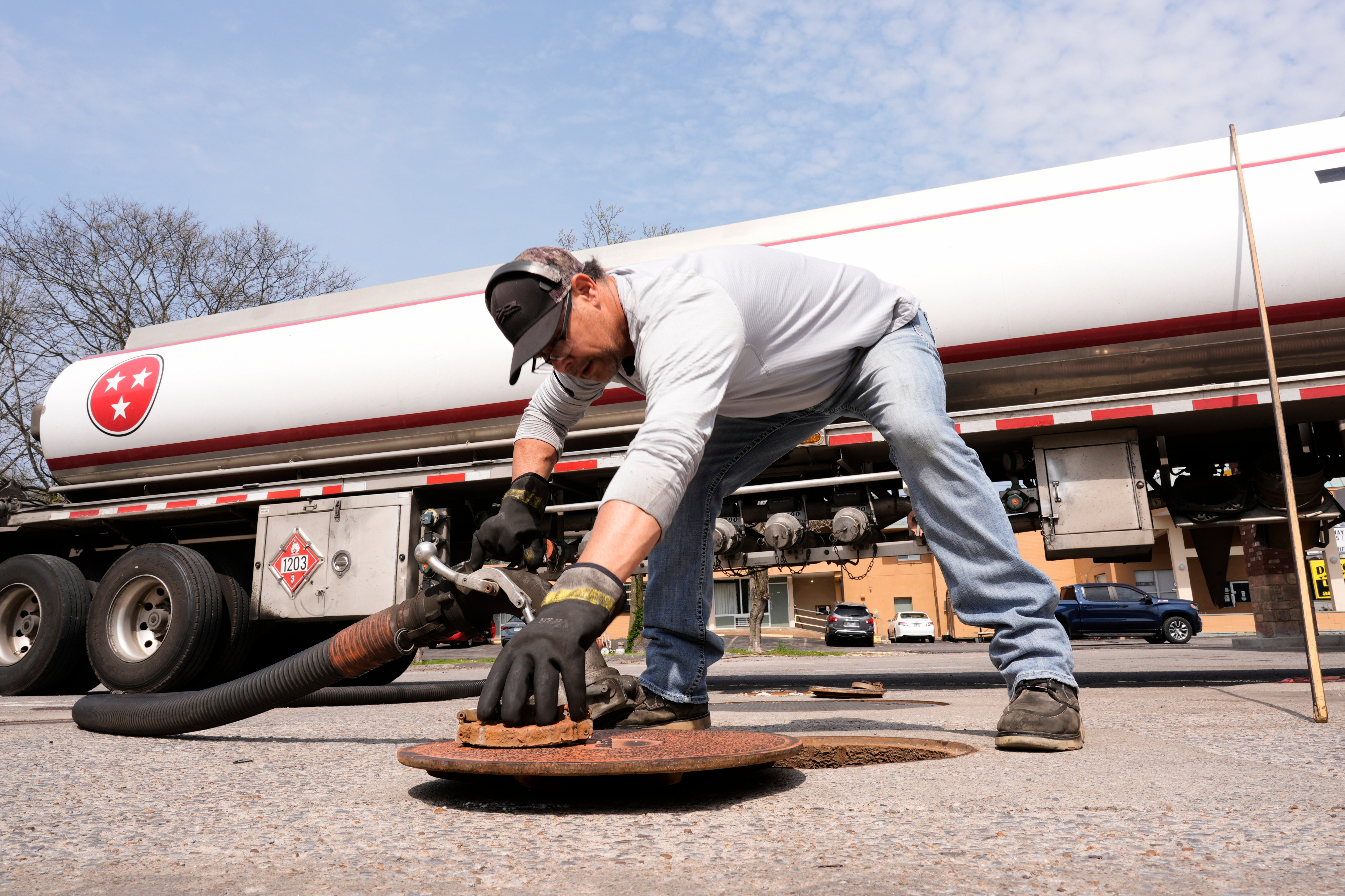 Worker in safety gear performing maintenance on a Sunoco fuel tanker truck at an industrial facility.