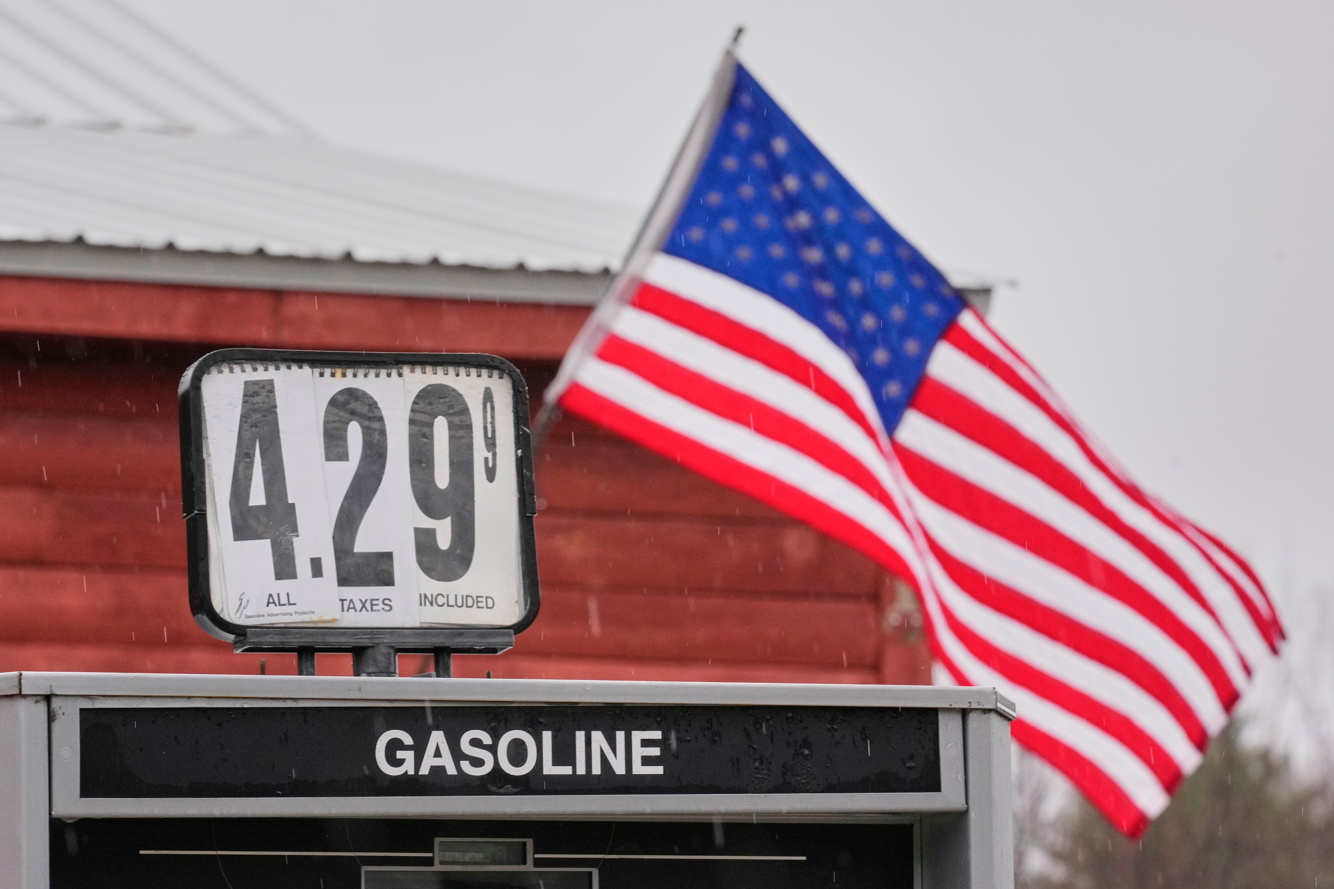 Gas station price sign displaying $4.29 per gallon with American flag flying in background