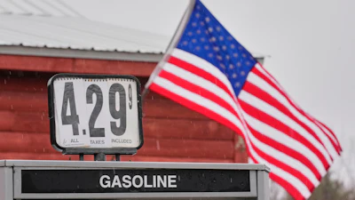 Gas station price sign displaying $4.29 per gallon with American flag flying in background