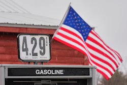 Gas station price sign displaying $4.29 per gallon with American flag flying in background