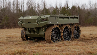 Olive green military six-wheel all-terrain truck with cargo bed parked on dirt terrain with bare trees in background