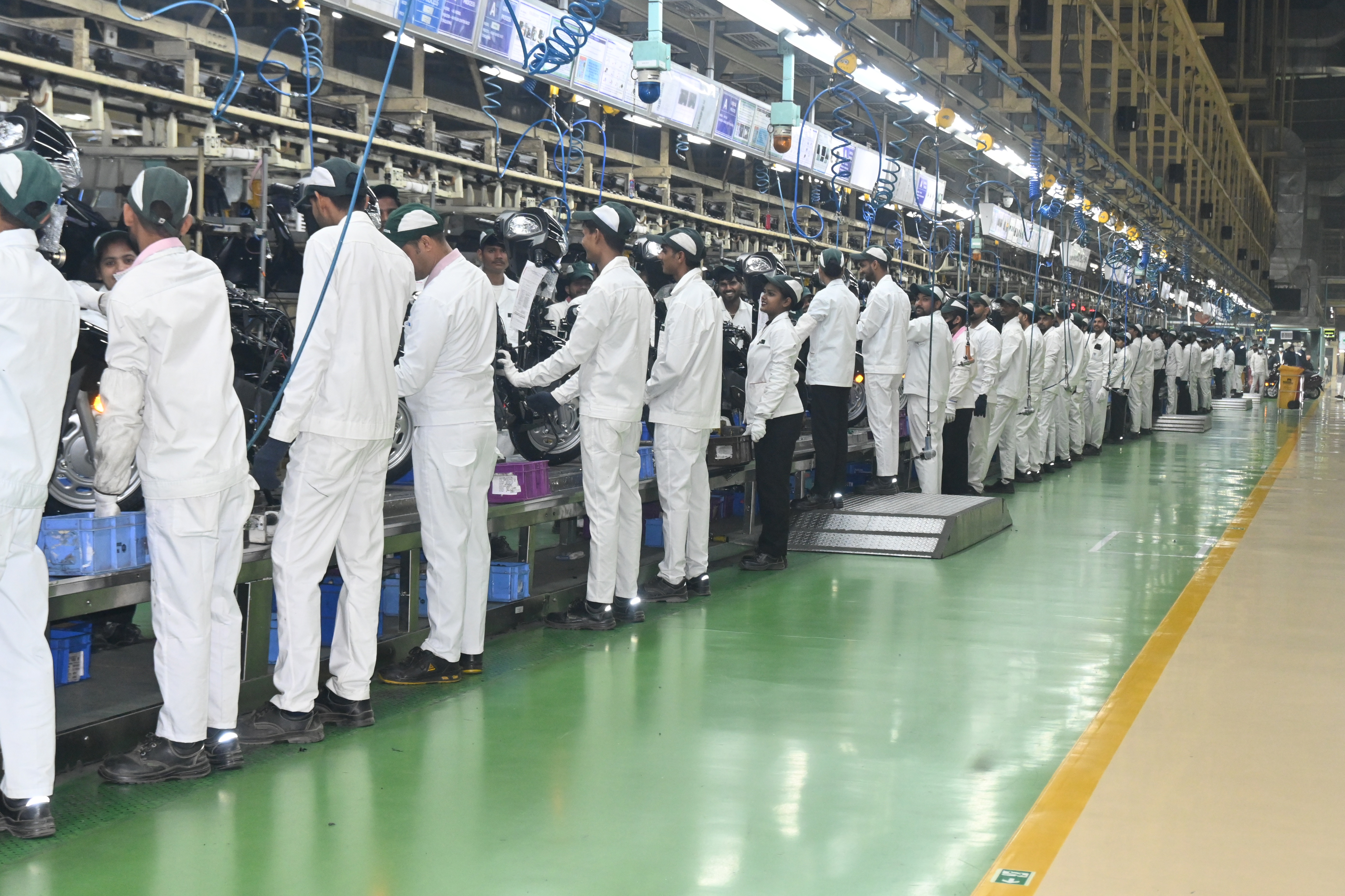 Factory assembly line with workers in white protective suits performing quality control at industrial workstations