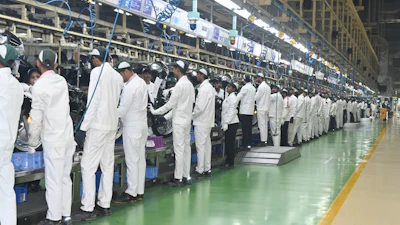 Factory assembly line with workers in white protective suits performing quality control at industrial workstations