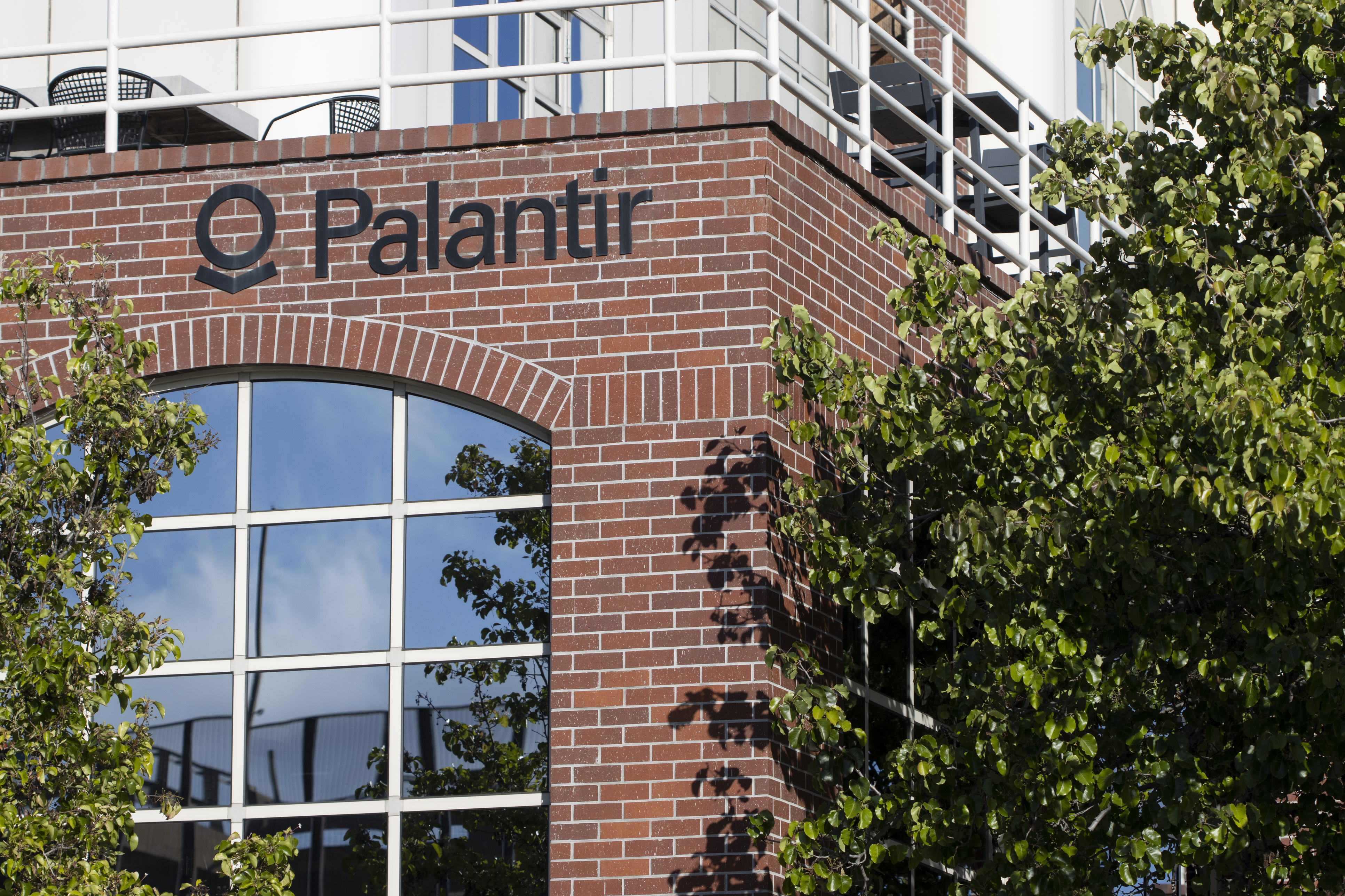 Palantir company signage on red brick building facade with large windows and climbing ivy