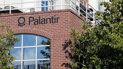 Palantir company signage on red brick building facade with large windows and climbing ivy