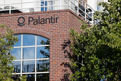 Palantir company signage on red brick building facade with large windows and climbing ivy