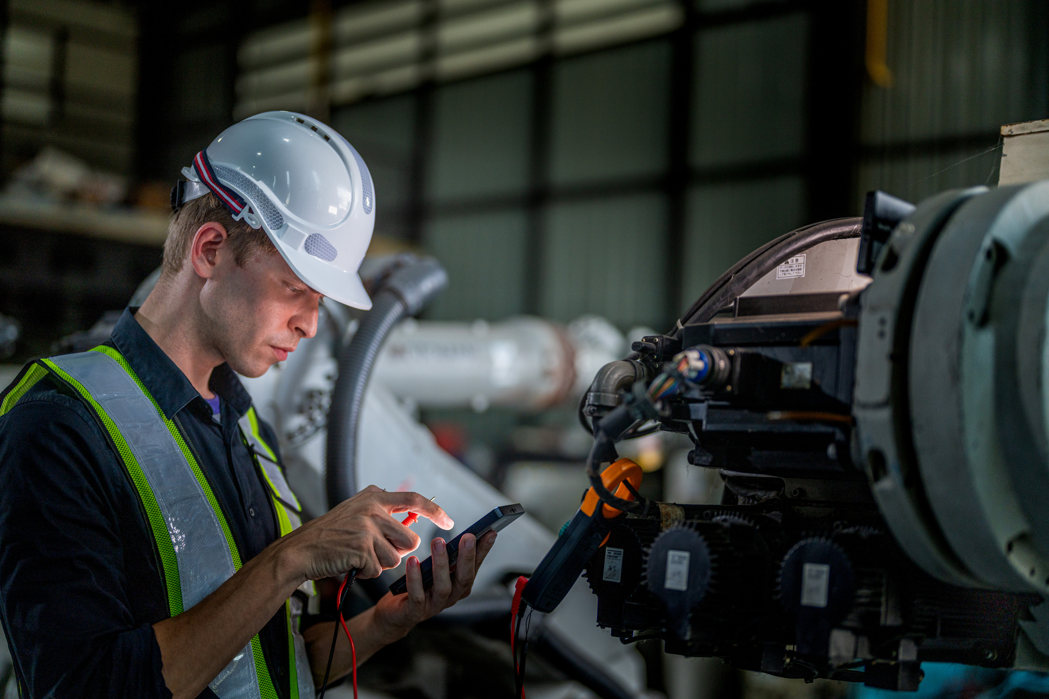 Industrial technician in safety gear inspecting equipment with diagnostic tool in factory setting