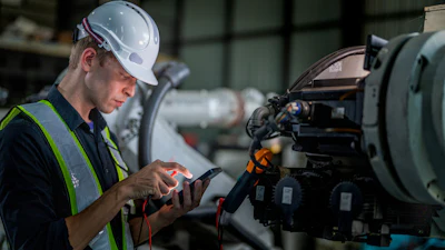 Industrial technician in safety gear inspecting equipment with diagnostic tool in factory setting