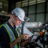 Industrial technician in safety gear inspecting equipment with diagnostic tool in factory setting
