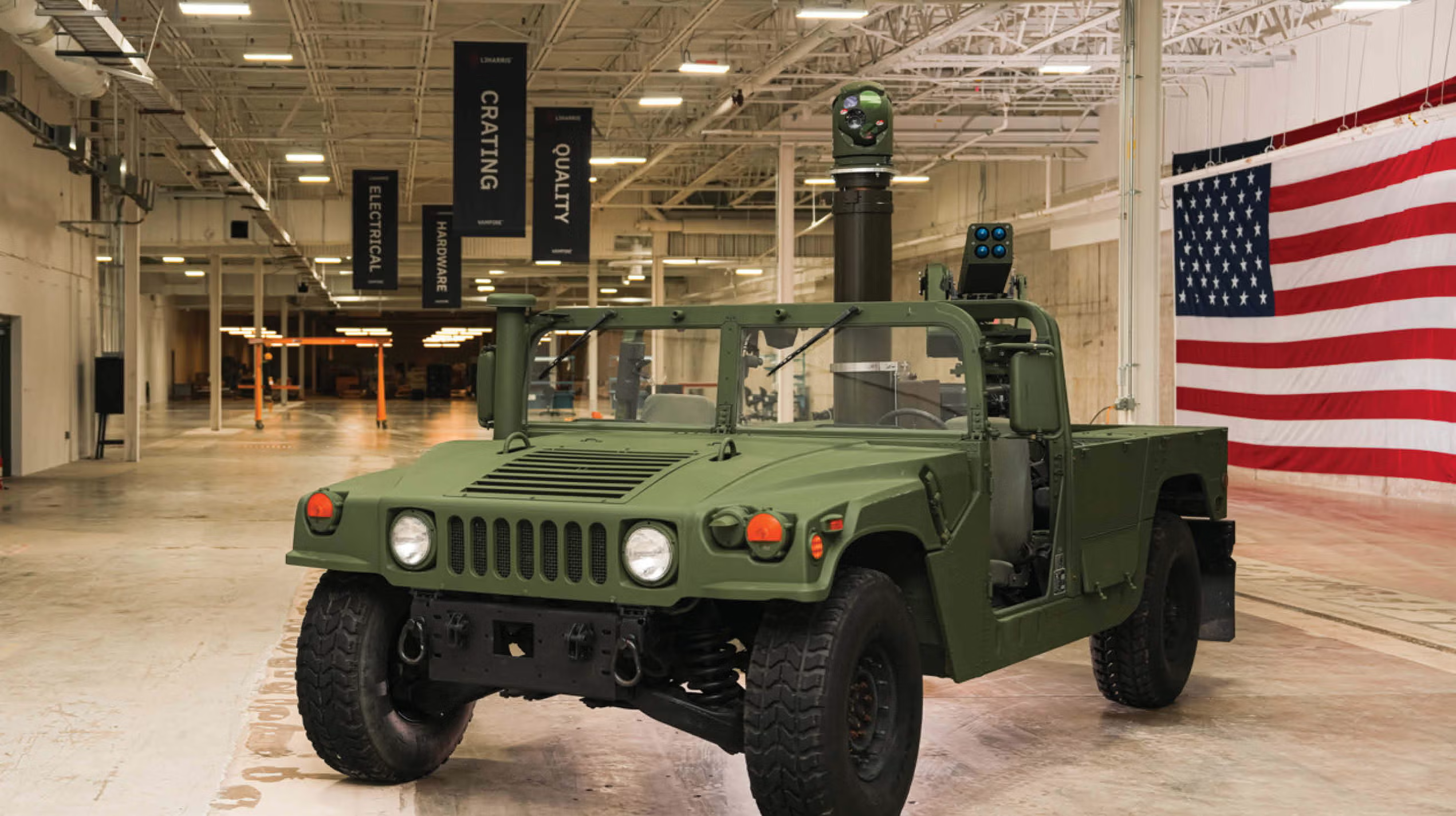 Olive green military Humvee on display in warehouse with American flag backdrop