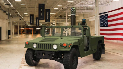 Olive green military Humvee on display in warehouse with American flag backdrop