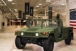 Olive green military Humvee on display in warehouse with American flag backdrop