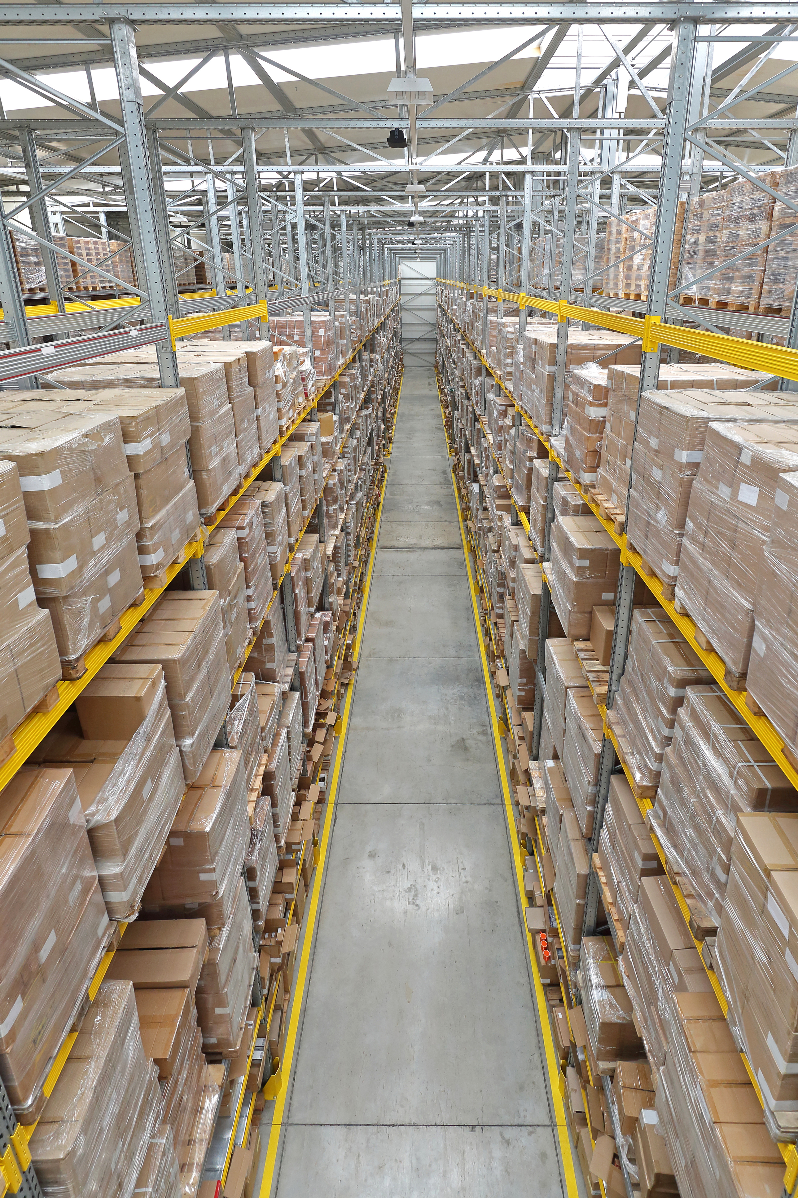 Industrial warehouse aisle with stacked cardboard boxes on metal shelving racks and yellow safety railings