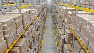 Industrial warehouse aisle with stacked cardboard boxes on metal shelving racks and yellow safety railings