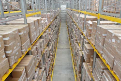 Industrial warehouse aisle with stacked cardboard boxes on metal shelving racks and yellow safety railings