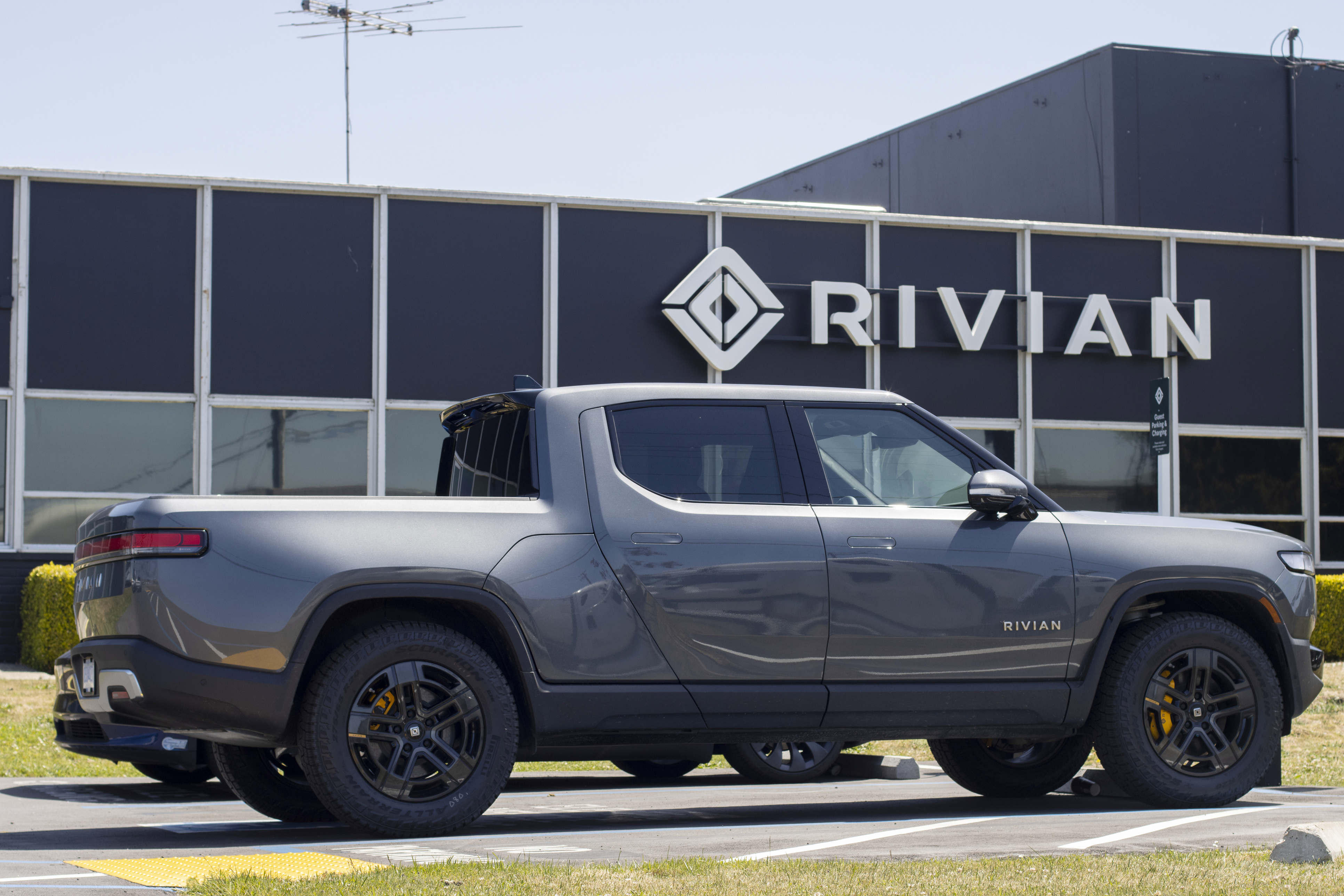 Gray Rivian R1T electric pickup truck parked in front of Rivian facility with company logo signage
