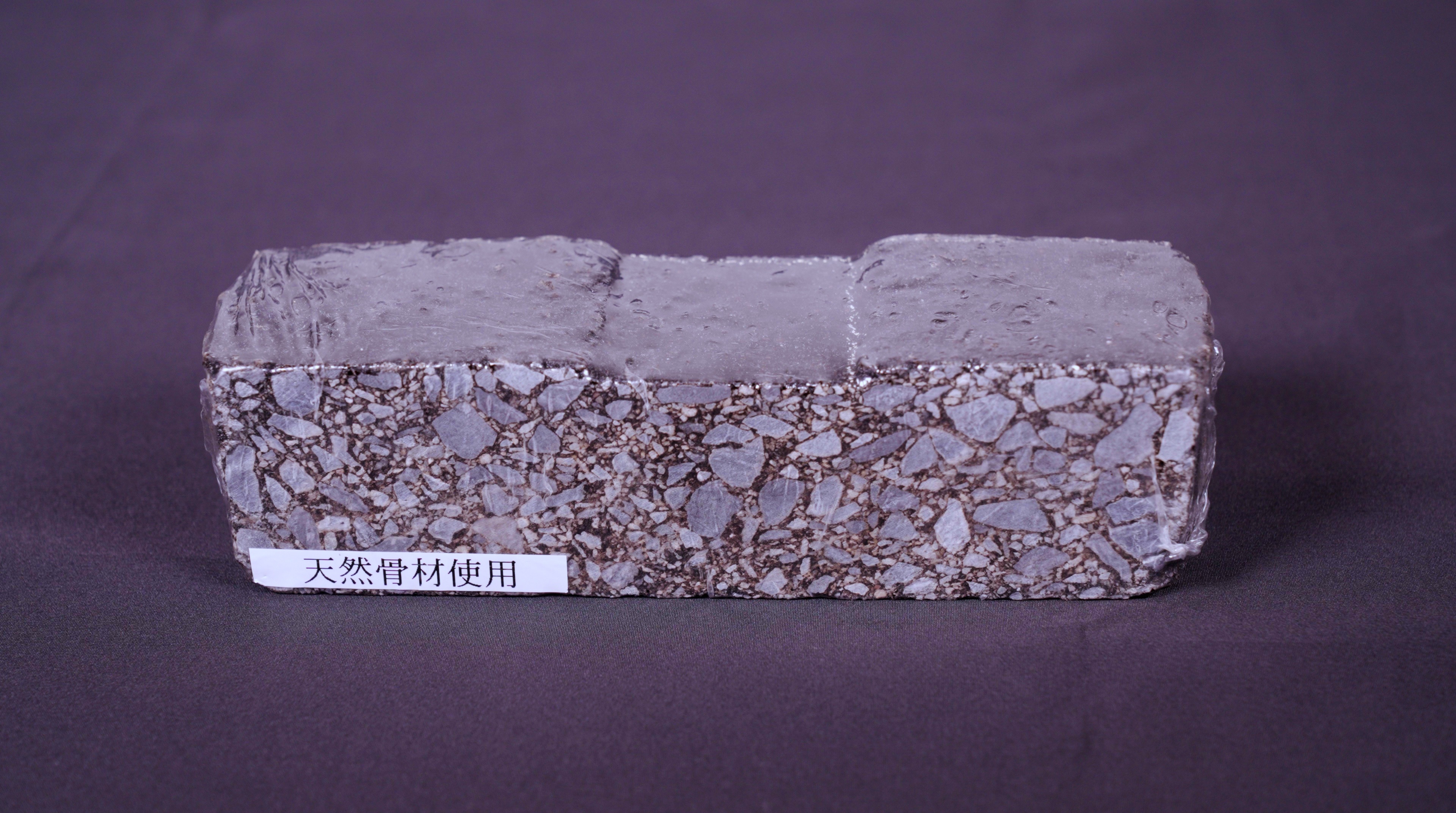 Rectangular composite brick sample with granular texture and smooth coating, labeled with natural material designation