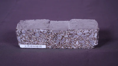 Rectangular composite brick sample with granular texture and smooth coating, labeled with natural material designation