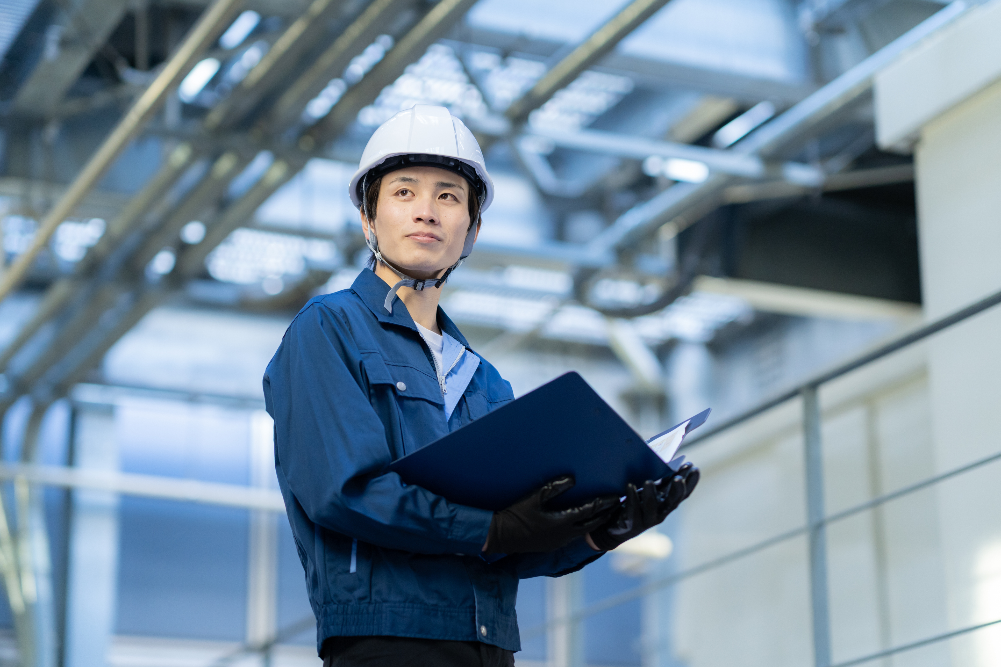Construction worker in hard hat and blue uniform holding clipboard in industrial facility